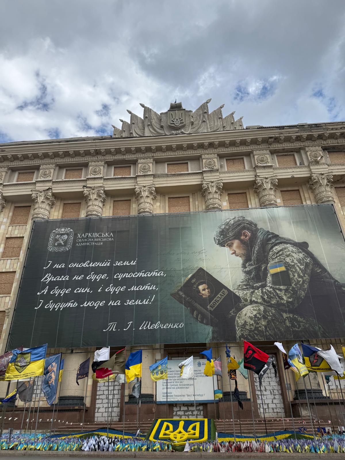 Foto des riesigen Rathaus-Gebäudes. Über nahezu die gesamte Fläche ist ein Plakat mit einem lesenden Soldaten gespannt. Im unteren Bildbereich, vor dem Gebäude, wurden sehr viele Flaggen für die gefallenden Soldaten der Stadt aufgestellt.