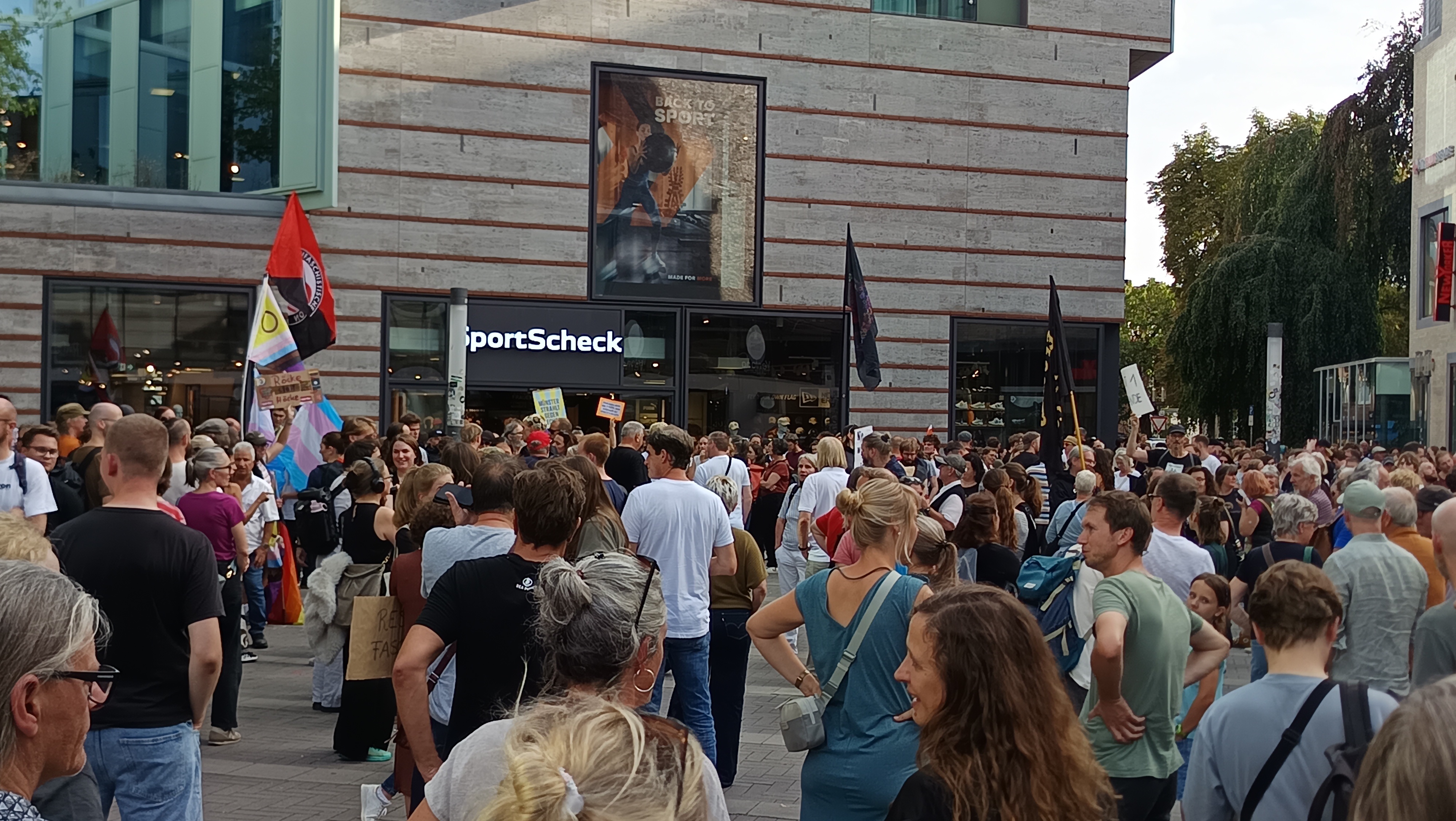 Foto einiger Menschen mit Flaggen und Sprüchen gegen rechts. Die Leute sind größtenteils bunt gekleidet.