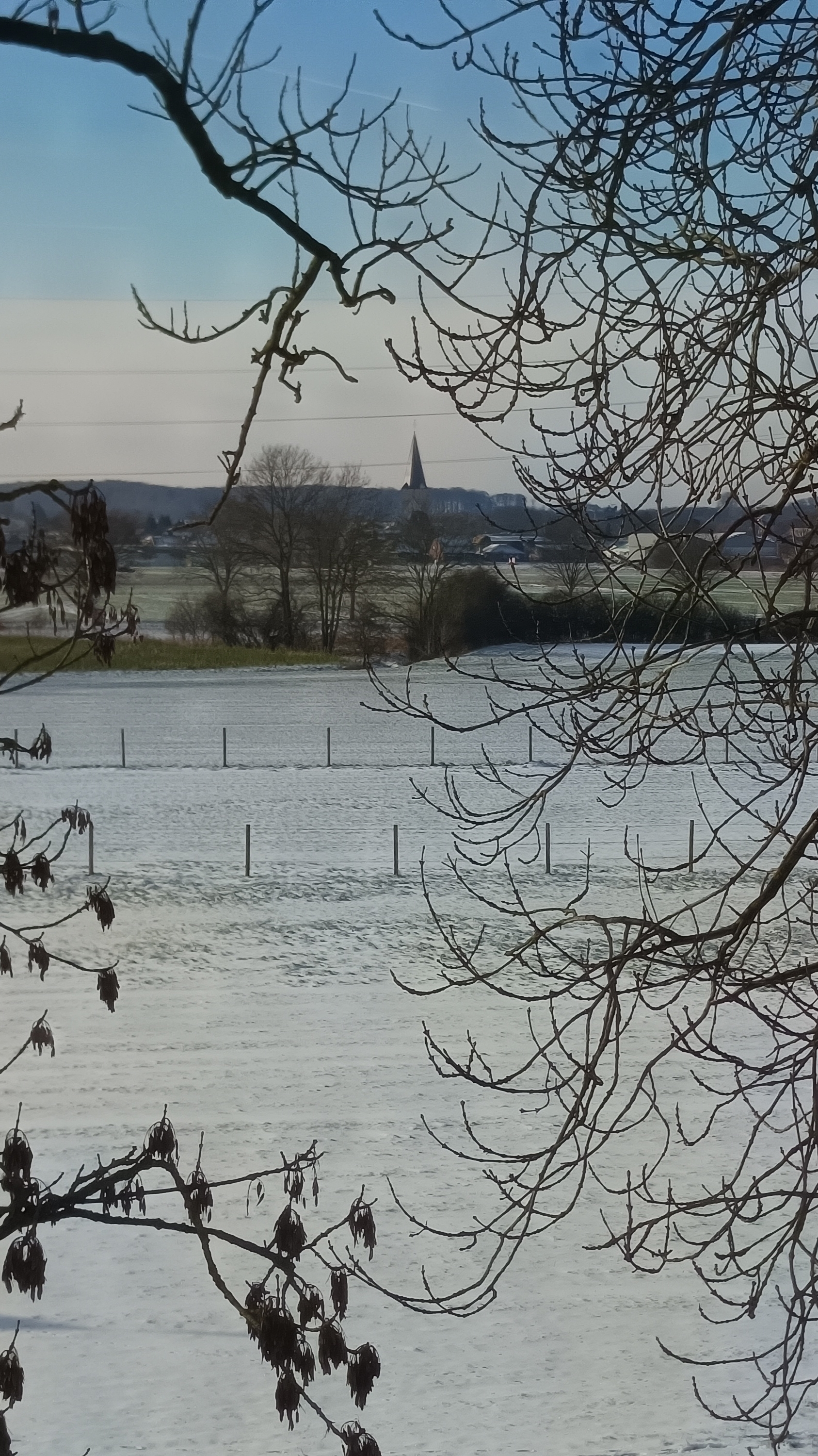 Foto von einer leicht verschneiten Landschaft. In der Ferne ist ein Kirchturm zu sehen.