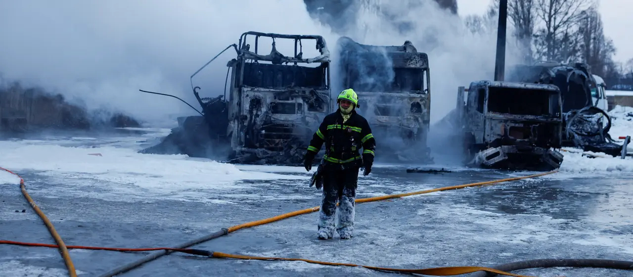 Ein Feuerwehrmann steht auf einem vereisten Parkplatz. Im Hintergrund sind mehrere ausgebrannte Fahrzeuge, die noch qualmen.